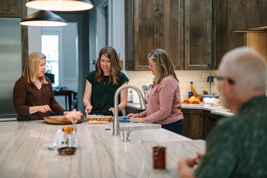 Abby slices baked goods at a kitchen island with her mother, Lisa, and her sister Angela as Steve sits nearby.