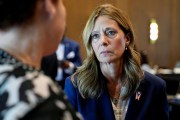 Amy Acton, wearing a navy blazer with an Ohio flag pin, listens intently to a person in the foreground.