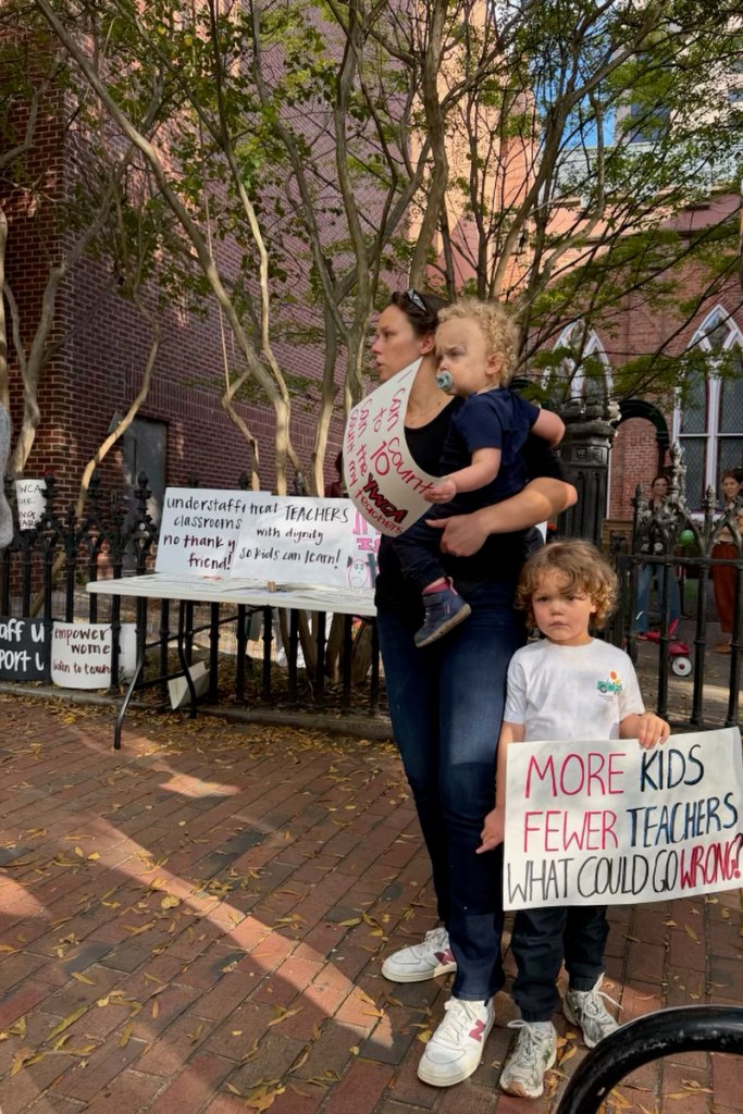 A parent and two children hold protest signs on a street.