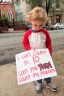 A child holds a protest sign on a street.