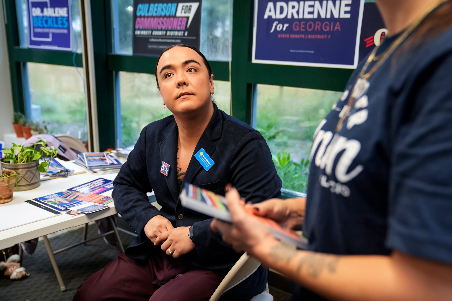 Hudgins sits in a chair listening to someone off frame and surrounded by campaign materials.