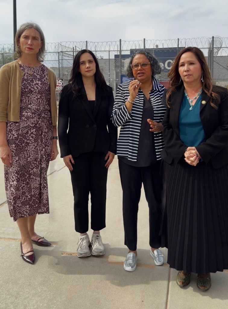 From left, Maxine Dexter, Yassamin Ansari, Mini Timmaraju and Adelita Grijalva stand outside the Eloy Detention Center in Arizona, in front of a chain-link fence topped with razor wire. Timmaraju gestures while speaking.
