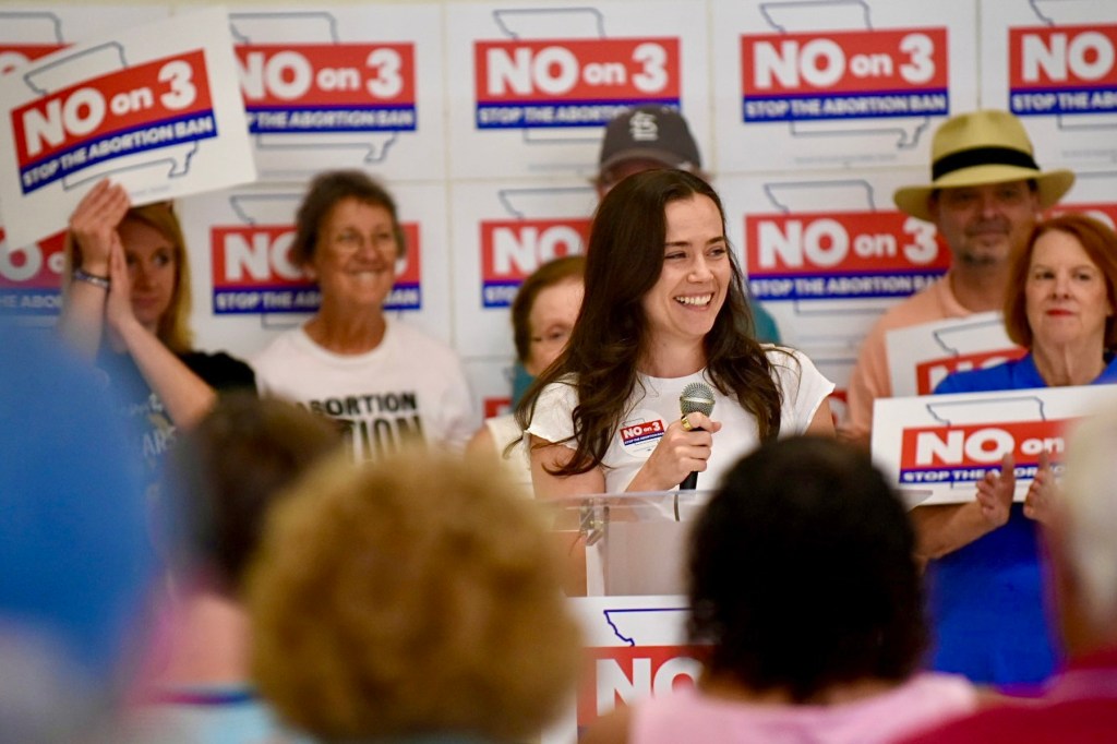 A woman stands among a crowd surrounded by signs saying No on 3.