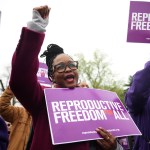 A protestor raises her fist while holding a sign for reproductive rights at a protest.