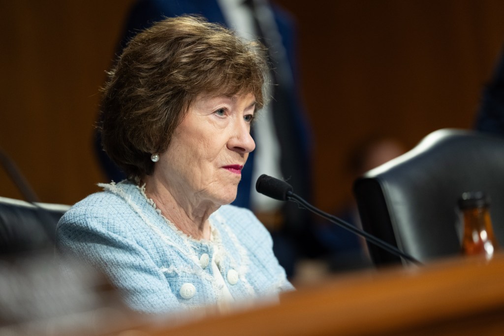 Collins seated at a table in front of a microphone.