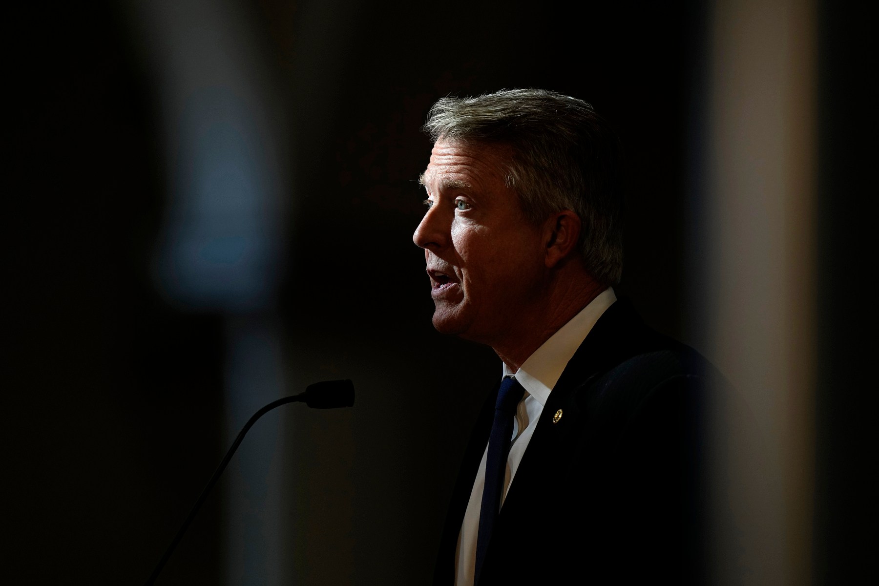 Marshall standing and speaking at a mic surrounded by darkness.