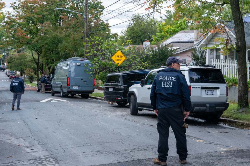HSI police stand on the street outside Omar's home with houses and cars in the background.