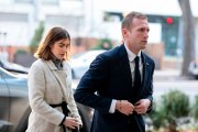 Max Miller, wearing a navy suit and tie, walks alongside Emily Moreno, dressed in a cream-colored coat, outside a building in Washington.