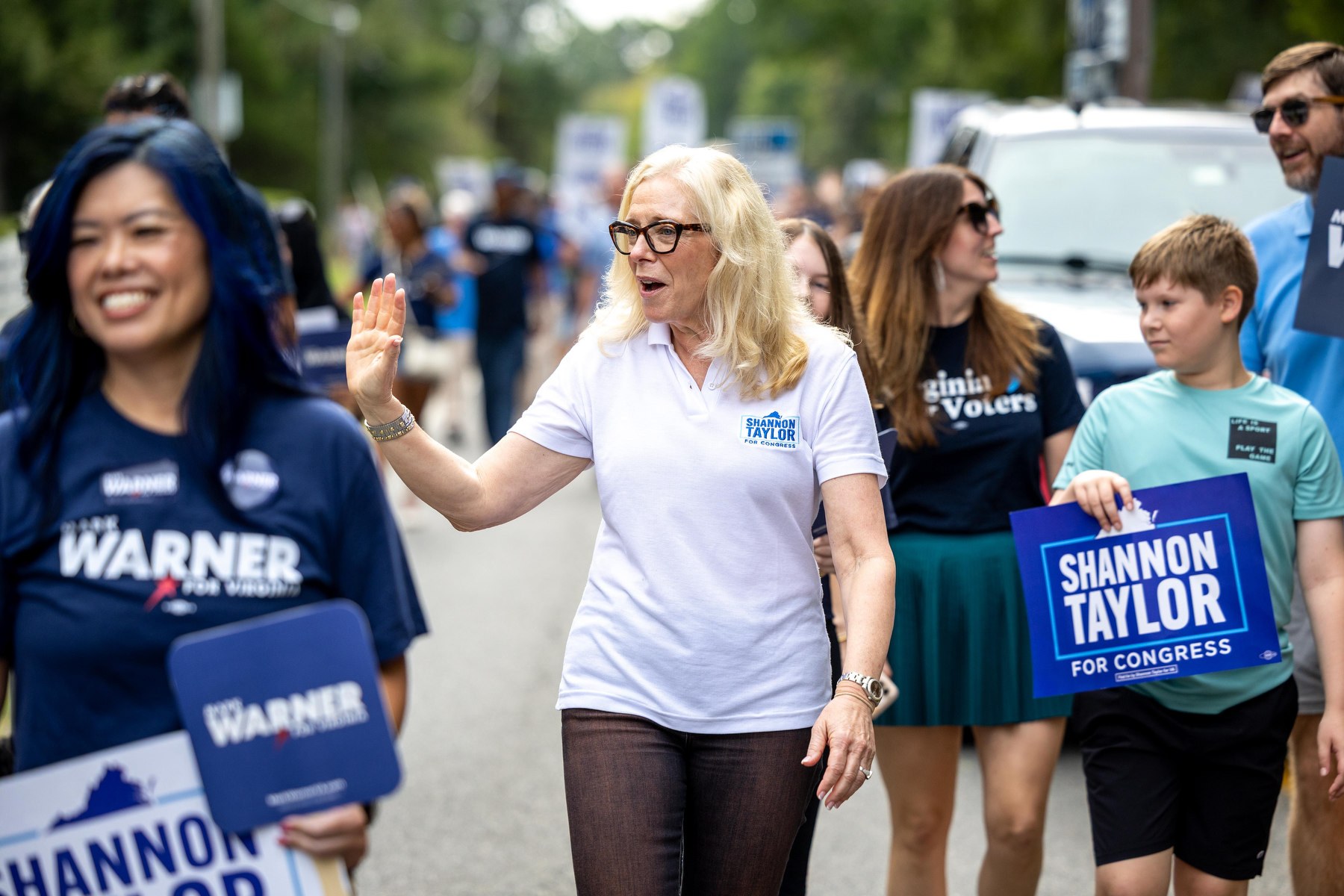 Taylor walks down the street waving while surrounded by people holding campaign signs.