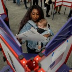 A voter holds a baby as she fills out her ballot during in-person voting at a polling place.