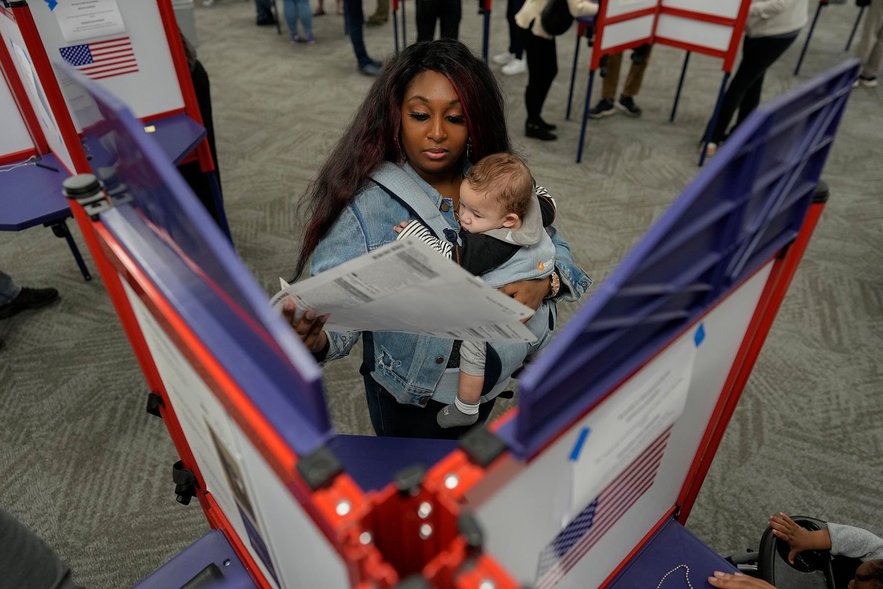 A voter holds a baby as she fills out her ballot during in-person voting at a polling place.